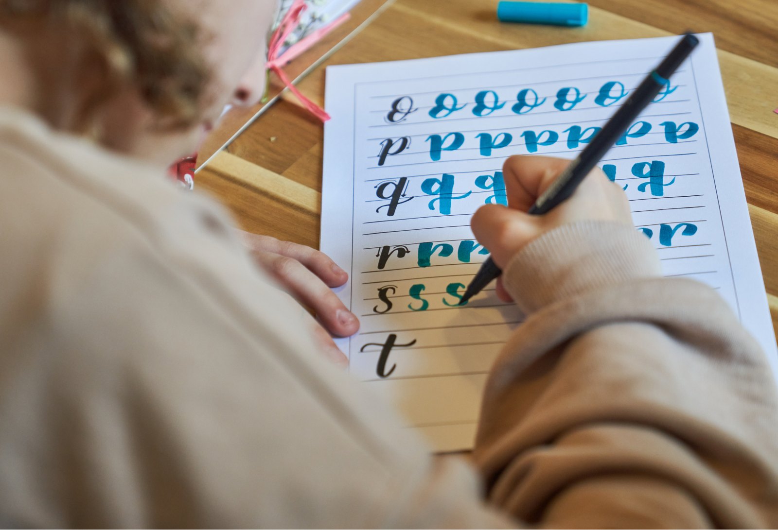 Beginner tracing teal brush letters on a practice worksheet