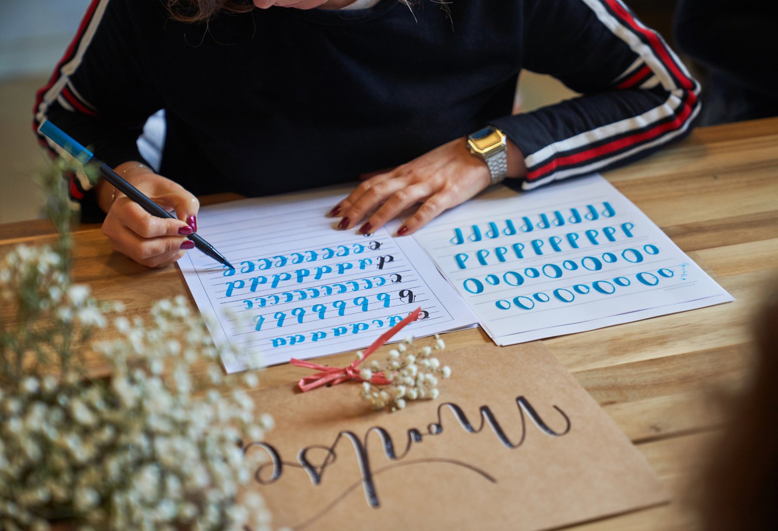 Watercolor lettering worksheets and a hand lettered card on a wooden table